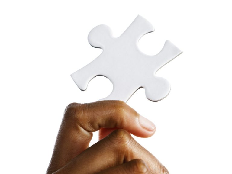 Die Hand eines dunkelhäutigen hält eine weißes Puzzleteil nach oben.